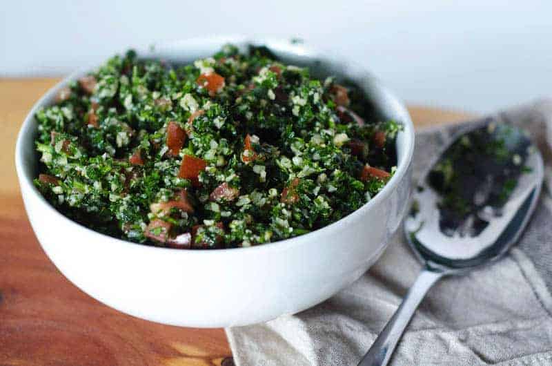 Side view of a white bowl full of cauliflower tabbouleh salad with a spoon and napkin