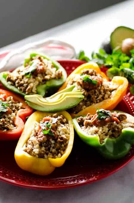 red plate with stuffed colored bell peppers topped with sliced avocado