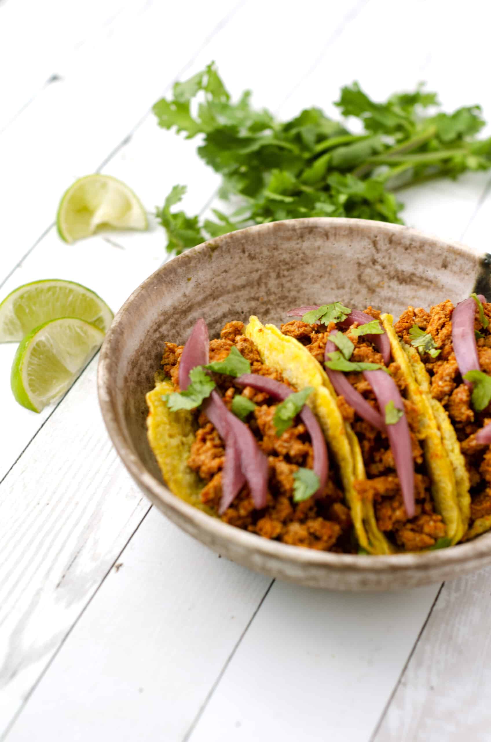 Side view of chorizo breakfast tacos in a bowl surrounded by lime slices and cilantro