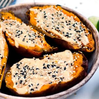 bowl of halved sweet potatoes topped with tahini spread and sesame seeds