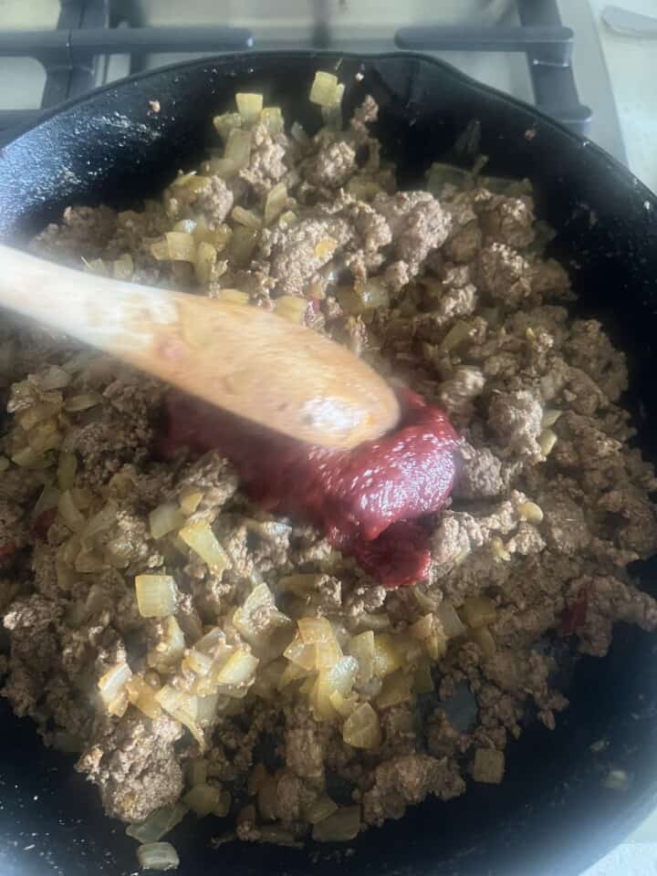 tomato paste and liquid seasonings added to pan of cooking meat