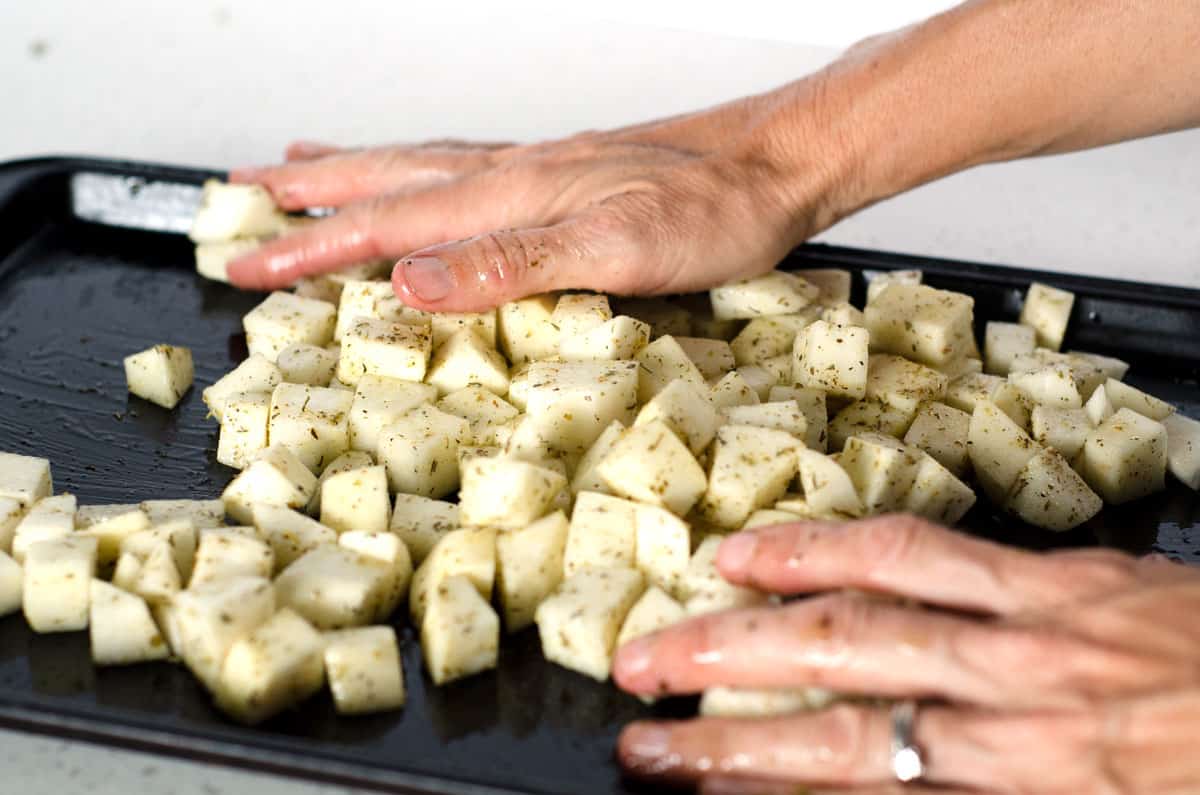 Sheet pan of raw turnips with hands tossing to coat in oil and seasonings