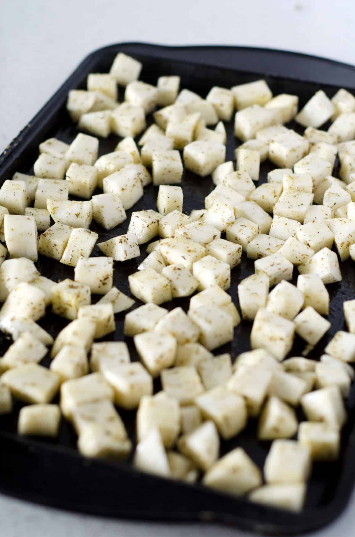 Raw turnip cubes on a baking sheet covered in seasoning and spread out