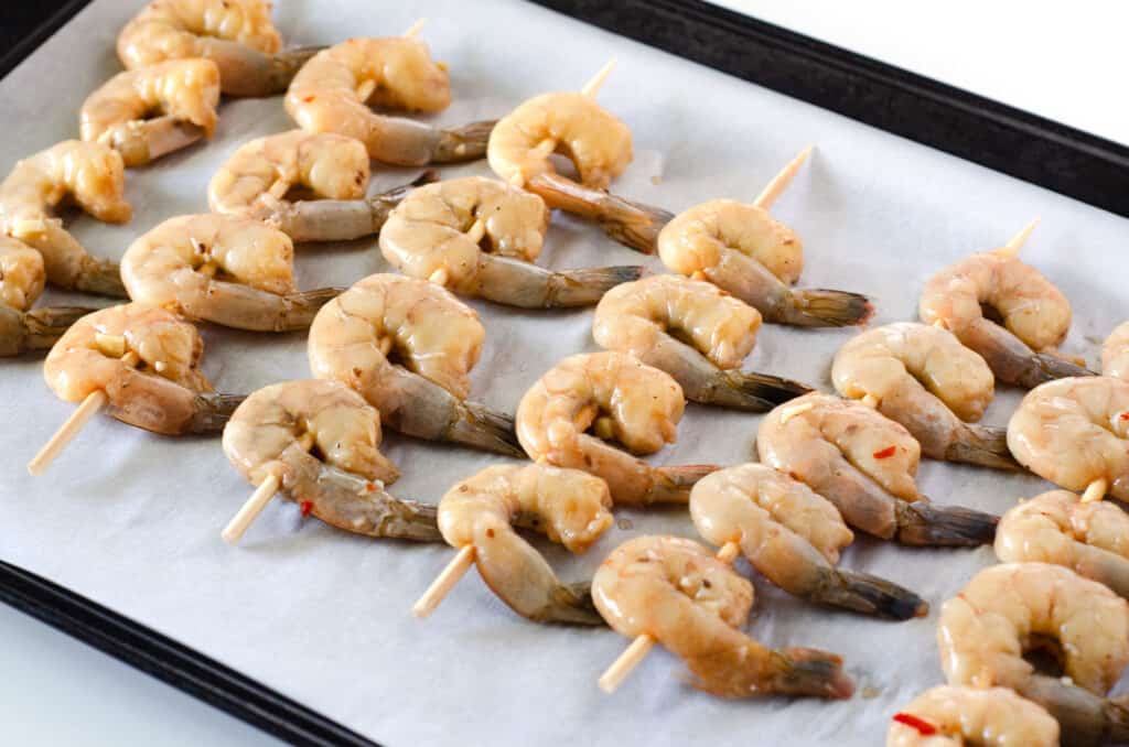 Shrimp skewered on a lined baking sheet before going into oven